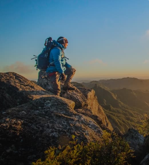 Dreamaroo Luxury, Man In Hiking Gear Kneeled On The Peak of A Mountain Watching The Sunset/Sunrise Image