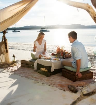 Dreamaroo Luxury, Honeymoon & Beautiful Islands Australia, Man and Woman Couple Sitting At Beach By Shore, Sharing Food Image