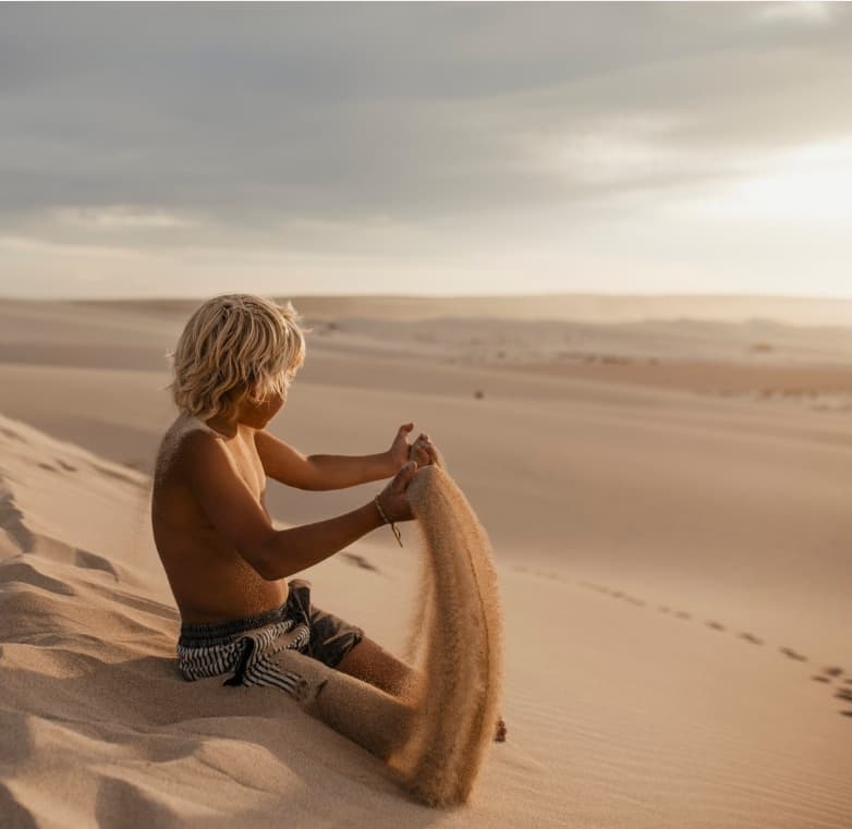 Dreamaroo Luxury, Blonde Little Boy Wearing Swim Trunks In Desert Playing With Sand Image